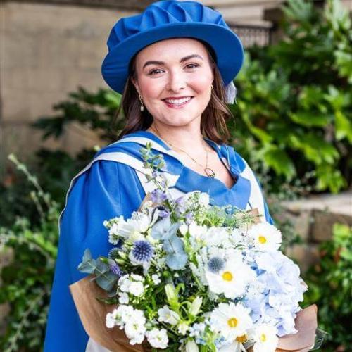 Lou May wearing Honorary Doctorate clothing, holding large bouquet of flowers