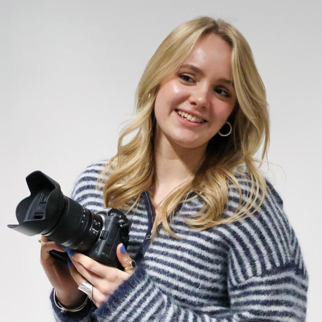 A female fashion photography student in a studio, holding a camera.