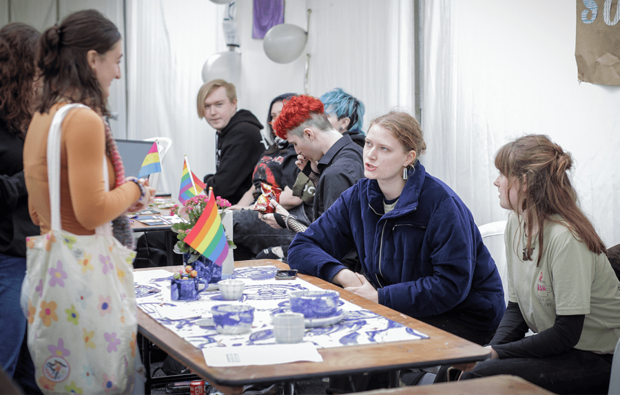 members of the ceramics society sit behind a table at the activities fair. They are talking to two interested students stood the other side of the table