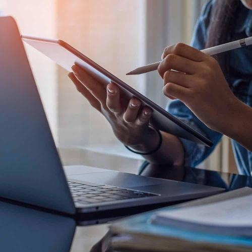 Person writing on computer tablet in front of a laptop