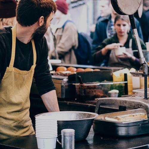 Young man at his food stall in a brown apron.