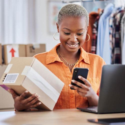 Woman with laptop, phone and parcel and a clothing rail in the background