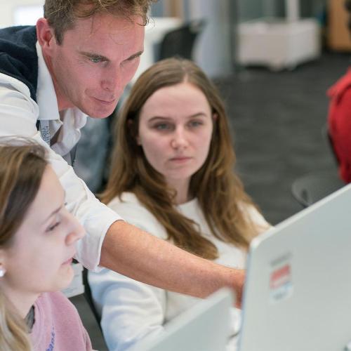Teacher and two students examining work on a screen in a computer lab
