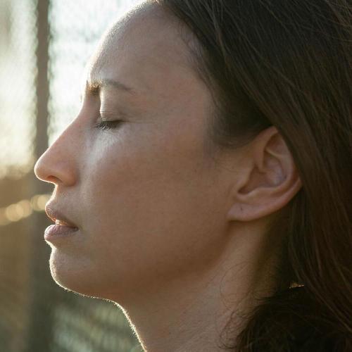 Woman with closed eyes leans her head against fencing