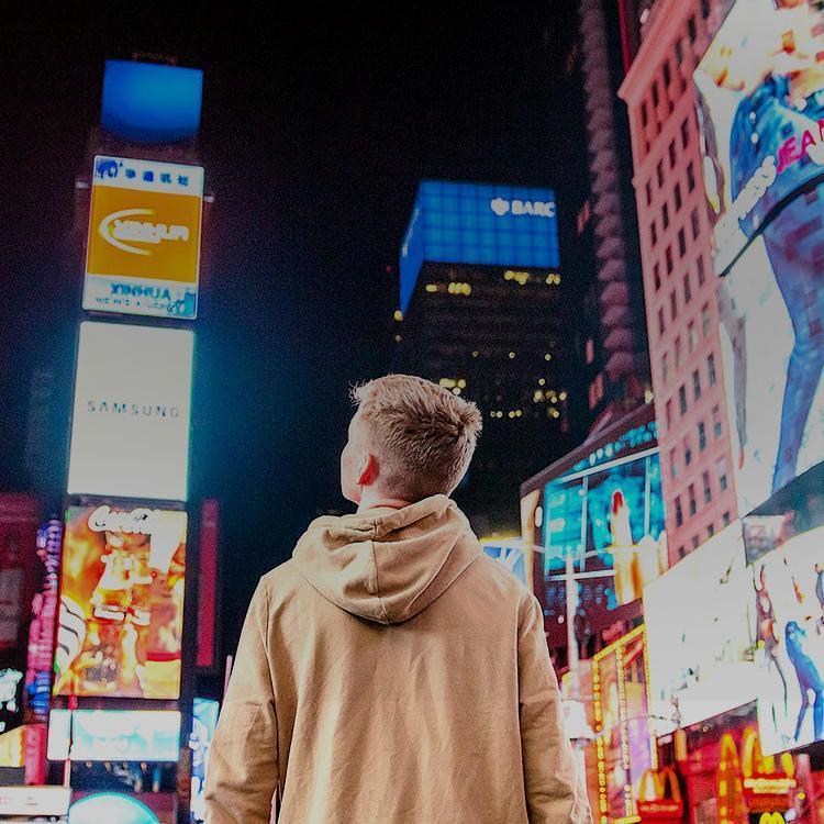 Young person in a beige hoodie looking at screens in Times Square