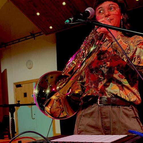 Student plays trumpet while standing near a laptop and electronic equipment