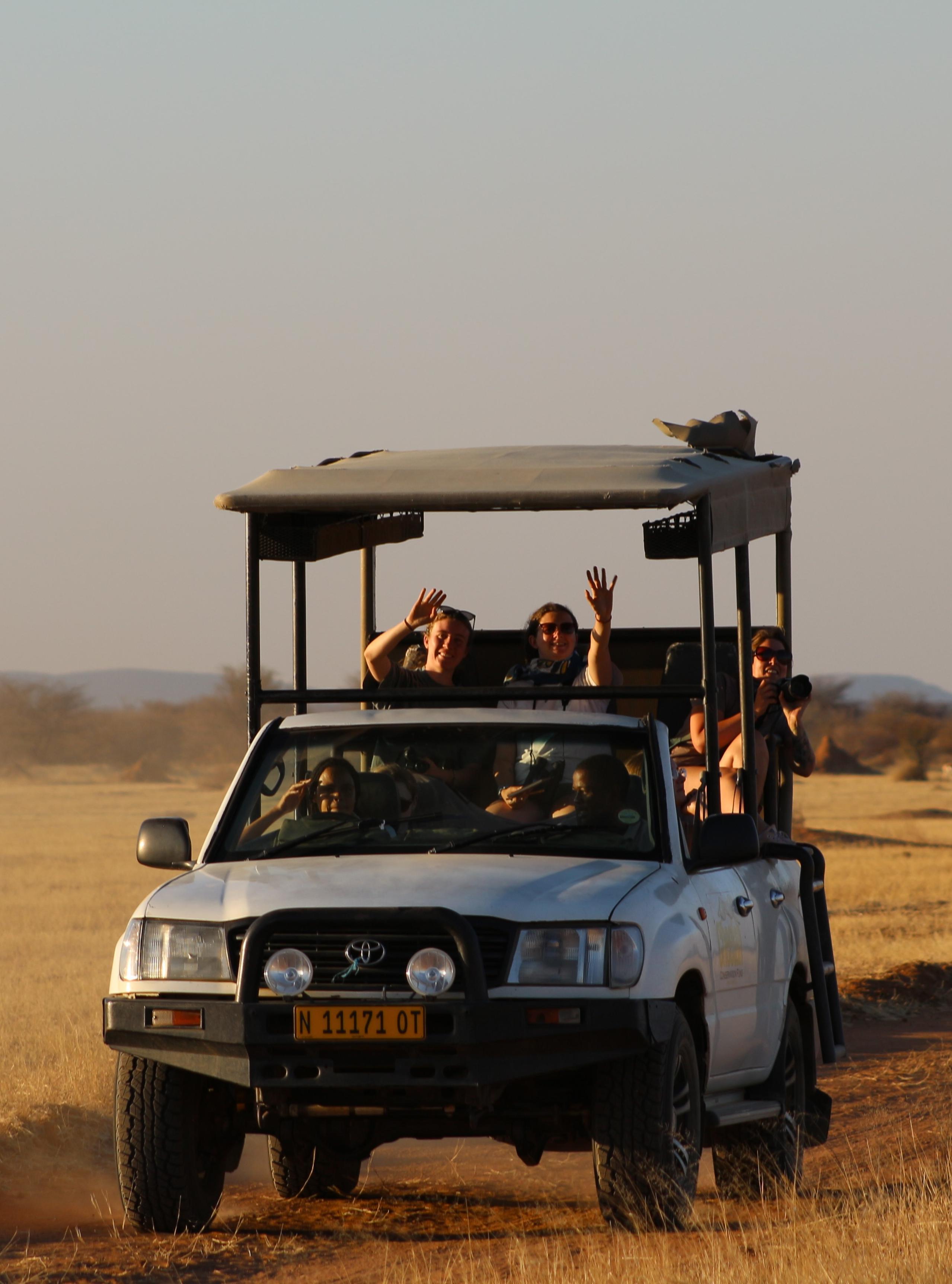 Students wave at the camera from a Jeep travelling through the desert