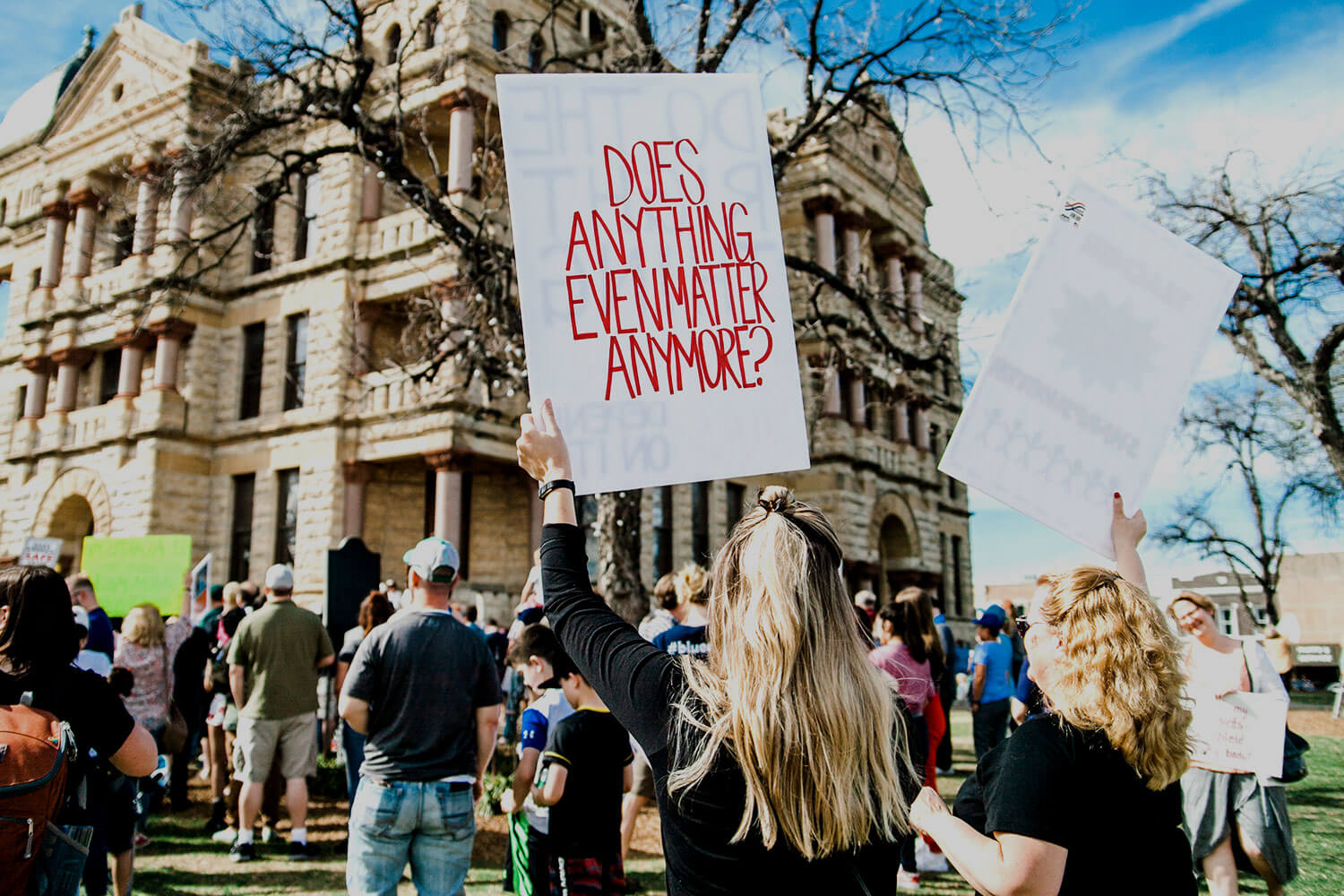Group of protesters outside a historic building. One holds a placard that says 