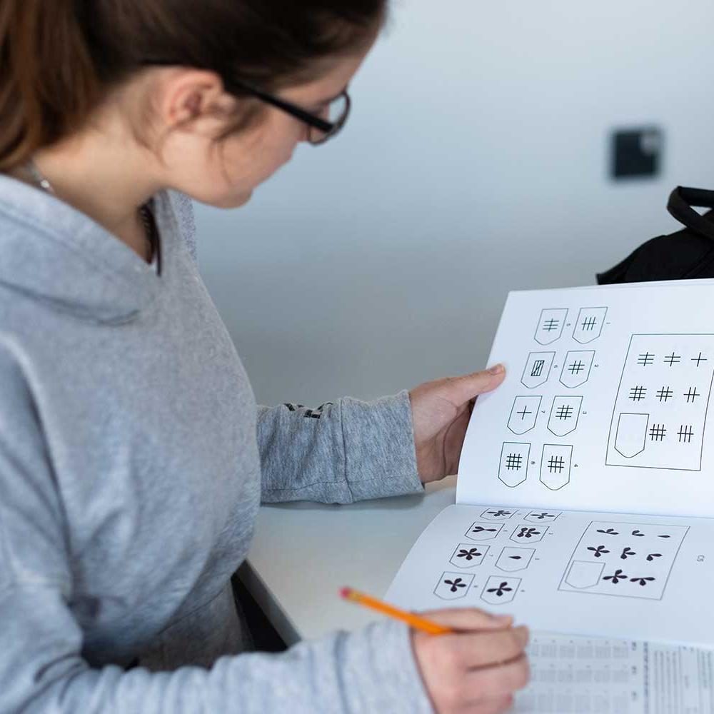 A student leans over a desk and completes a workbook