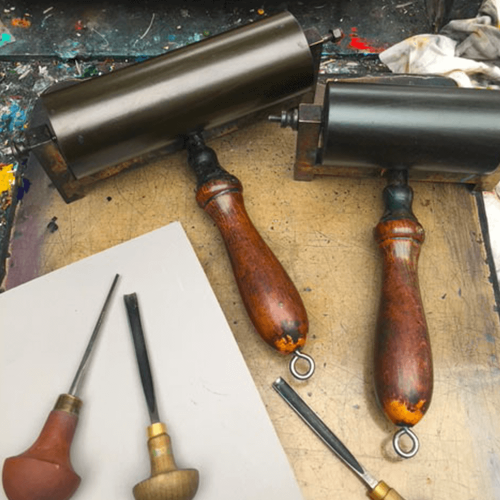 A selection of chisels and ink rollers laid on top of a lino block