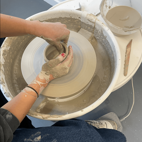 A pair of hands pinching a pot on a pottery wheel.