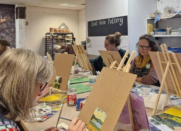 Photograph of group of people in painting workshop. Woman in foreground focused on fine detail brushwork