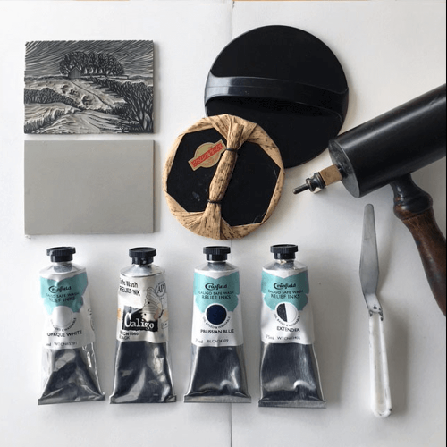 A flat lay of a lino block, inks and linocutting tools
