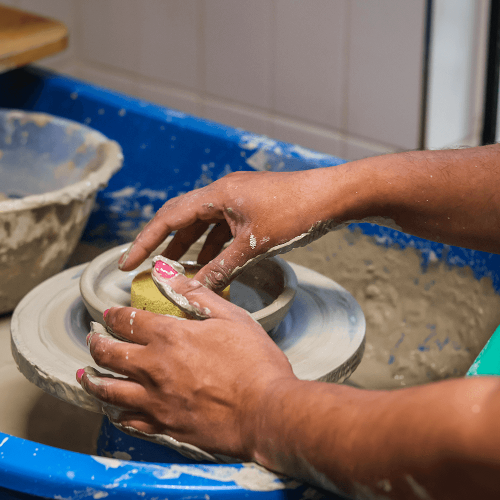 A person sat at a pottery wheel smoothing out a bowl with a sponge