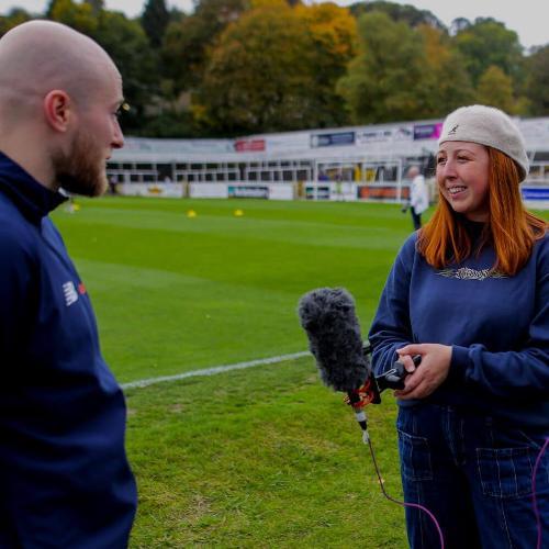 Student with mic talking with sports professional on a pitch