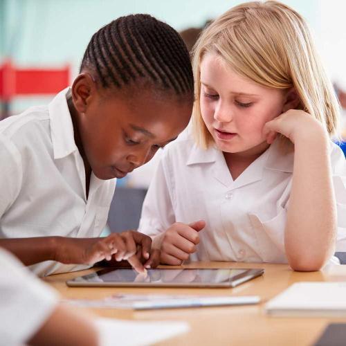 Two children in uniform working in a classroom setting on a tablet
