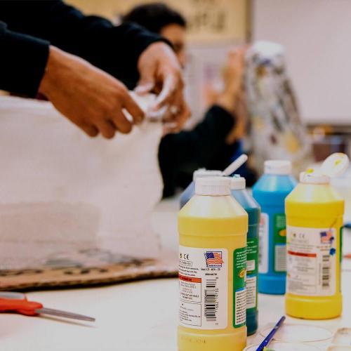 Bottles on paints on a table with students working in the background.