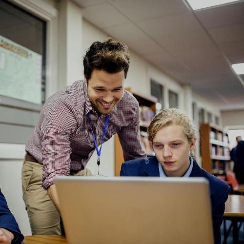 Teen students working on a laptop with teacher helping them.