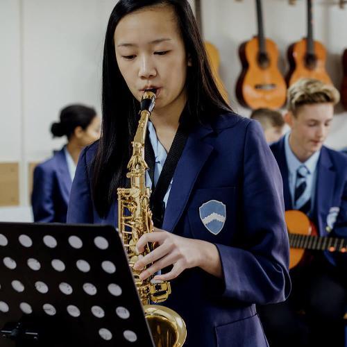 Teen student playing the saxophone in school music lesson.