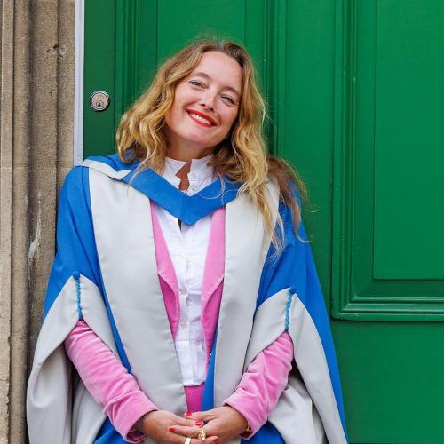 Person in ceremonial robes standing in front of a door smiling.