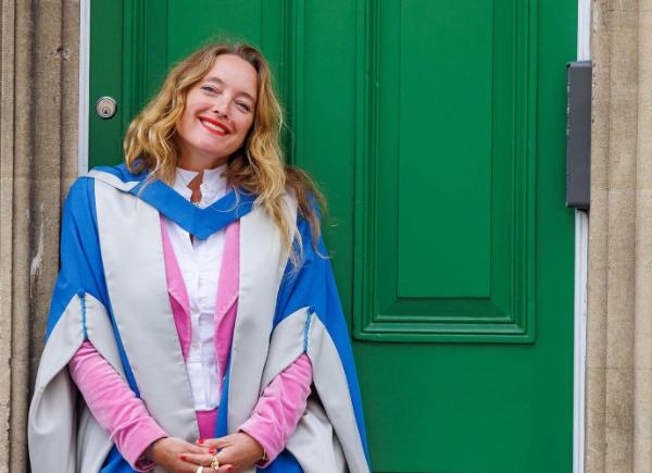 Person in ceremonial robes standing in front of a door smiling.