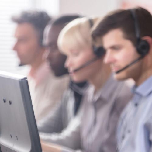 people sat at a long table wearing headsets and looking at computer screen