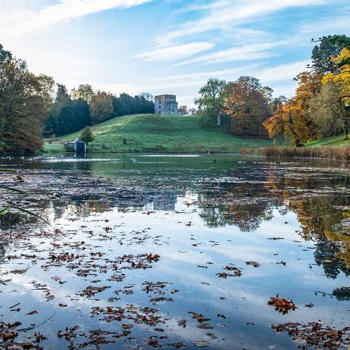Newton Park lake with blue skies and the castle at the top of the hill