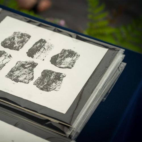 a black and white print of Stanton Drew stone circle in a black frame. Multiple are piled up on a table with greenery in background.
