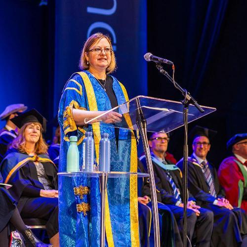 A woman stands on stage in academic robes 