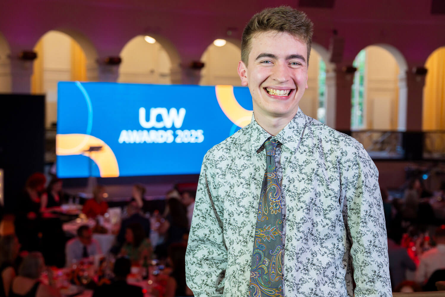 A male student stood in front of a screen that reads UCW Awards 2025