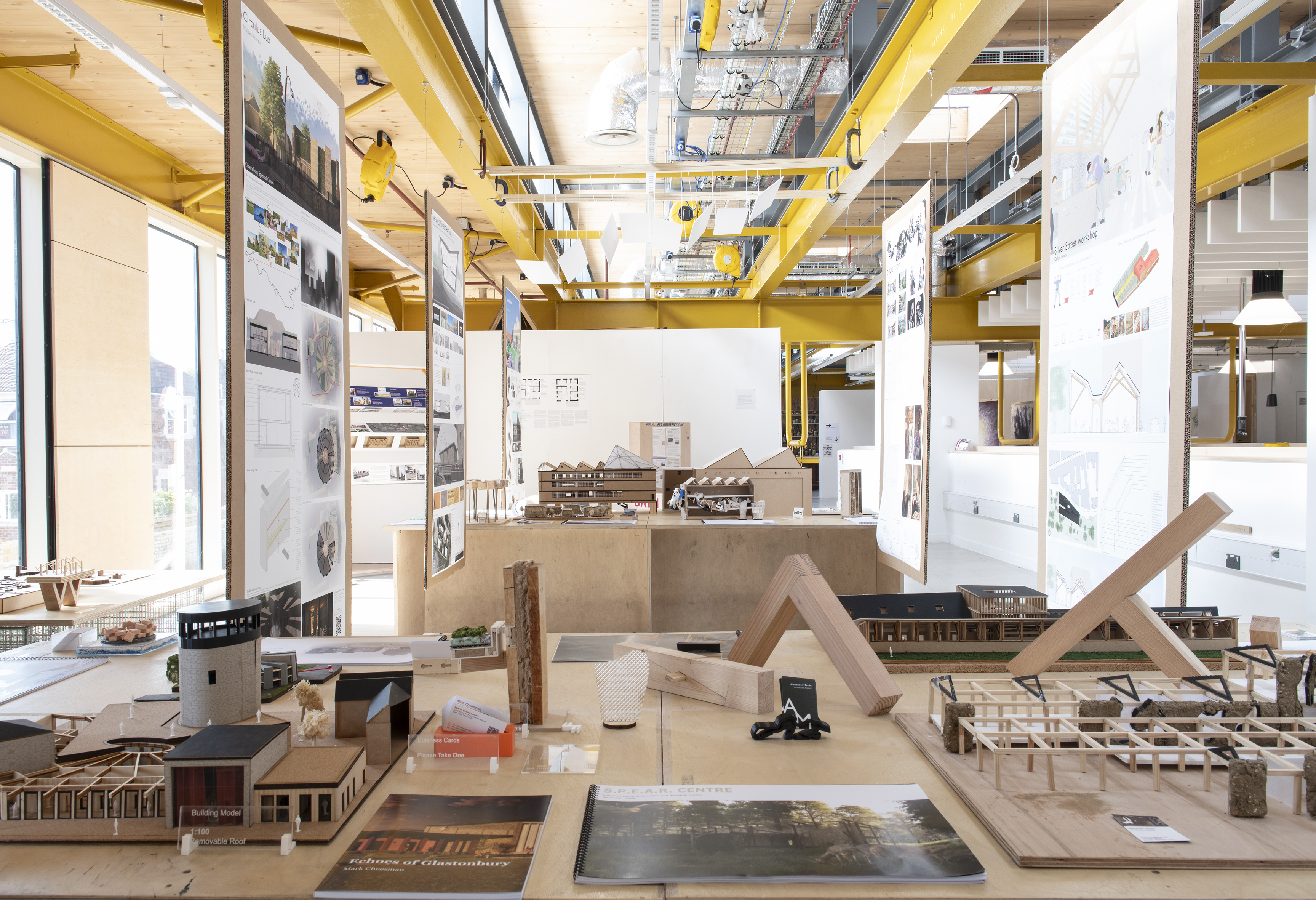 An exhibition space showing Architecture students' work handing from the ceiling and laid on tables
