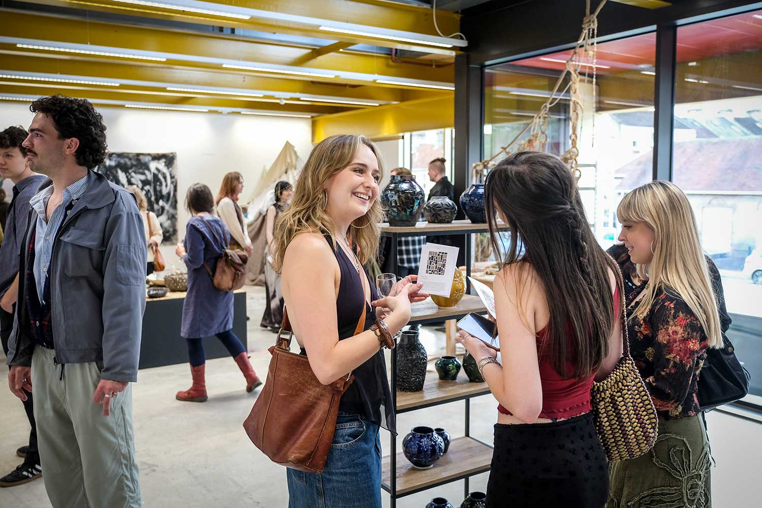 A bustling exhibition with ceramic works on display and students taking a closer look
