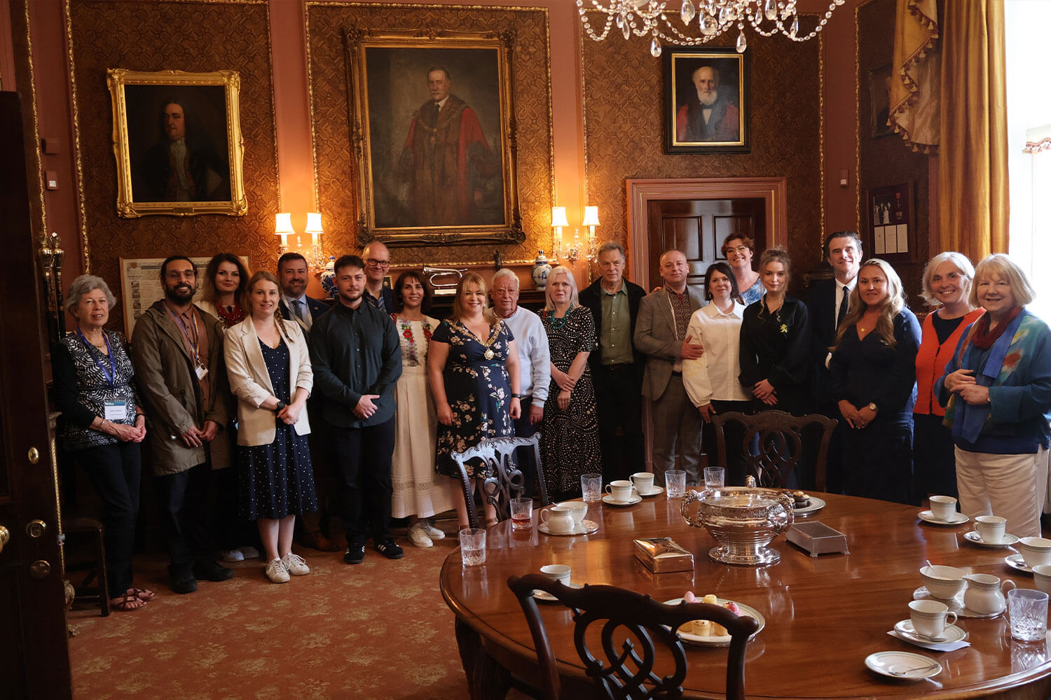 A group of people stood in a grand room with paintings on the walls, all looking at the camera and smiling