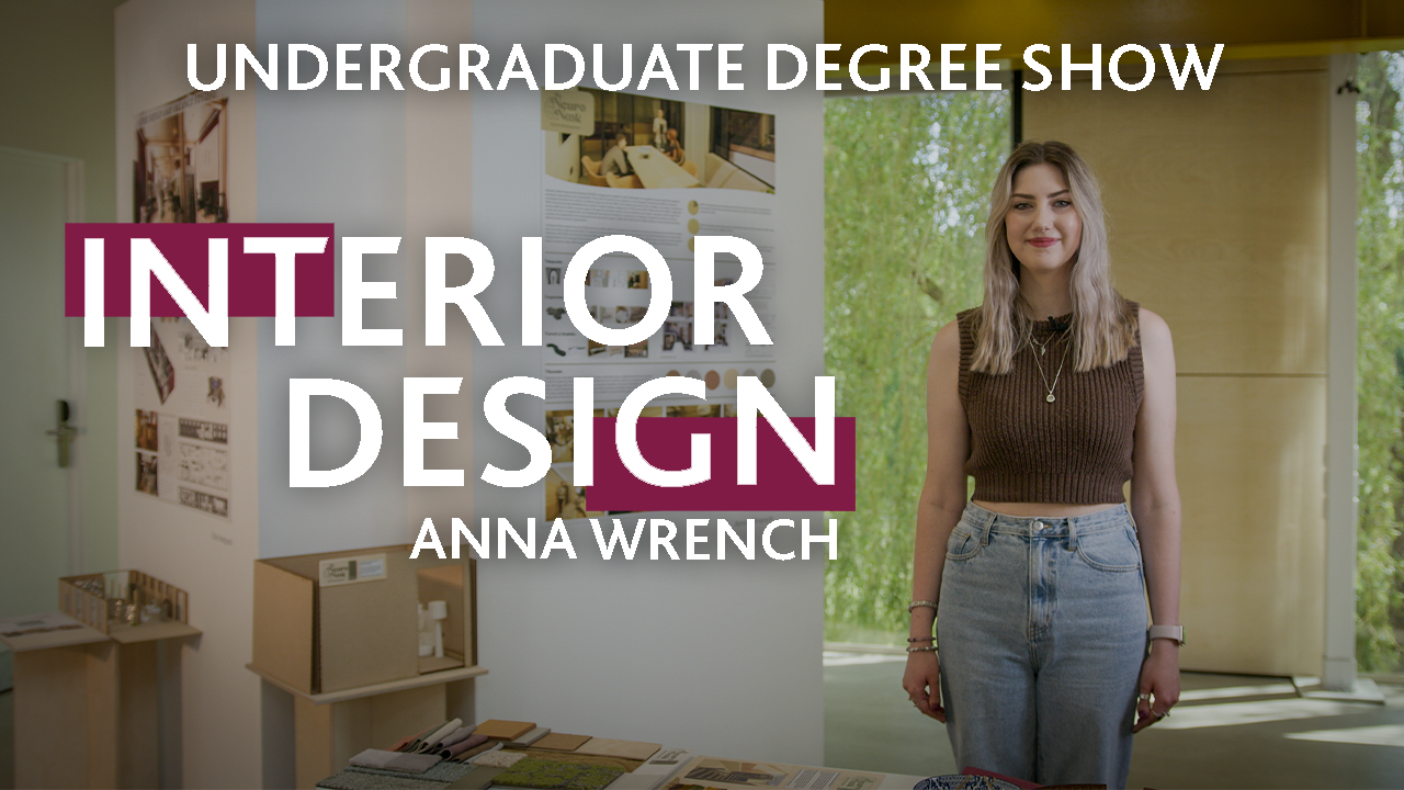 A person stands next to their Interior Design project exhibition with text that reads: Anna Wrench, Interior Design, Undergraduate Degree Show