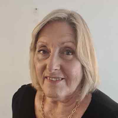 Person with shoulder length blonde hair in a black top with a gold necklace