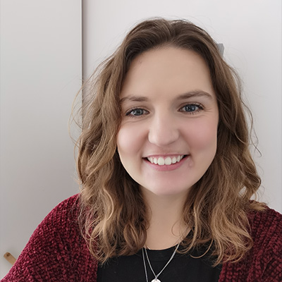 Headshot of smiling person with long wavy dark hair in burgundy top