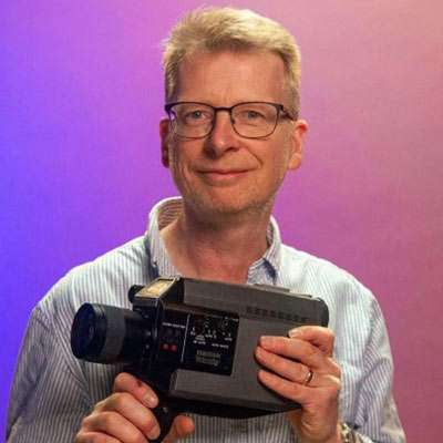 Person with short hair and glasses holding camera