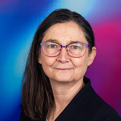 Person with long dark hair and glasses in black blazer smiling