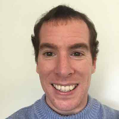 Person with short dark hair in blue jumper smiling at camera