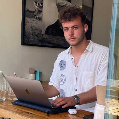A student wearing a white shirt looks at the camera while using their laptop