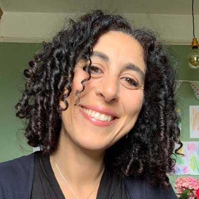 A person with dark curly hair smiles at the camera