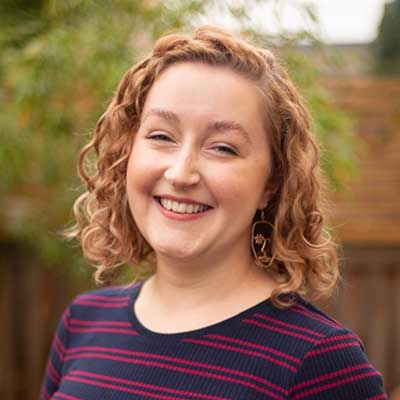 A person wearing a striped top with strawberry blonde hair smiles at the camera