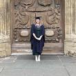 A person wearing navy graduation robes stands in front of a large ornate door outside Bath Abbey