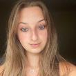 A person with long light brown hair looks at the camera