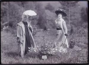 Two women one with parasol in traditional dress in a field
