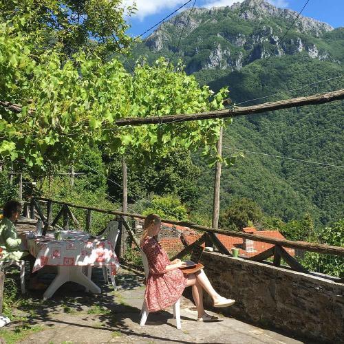 Person in long pink dress sitting writing on a terrace in leafy mountains