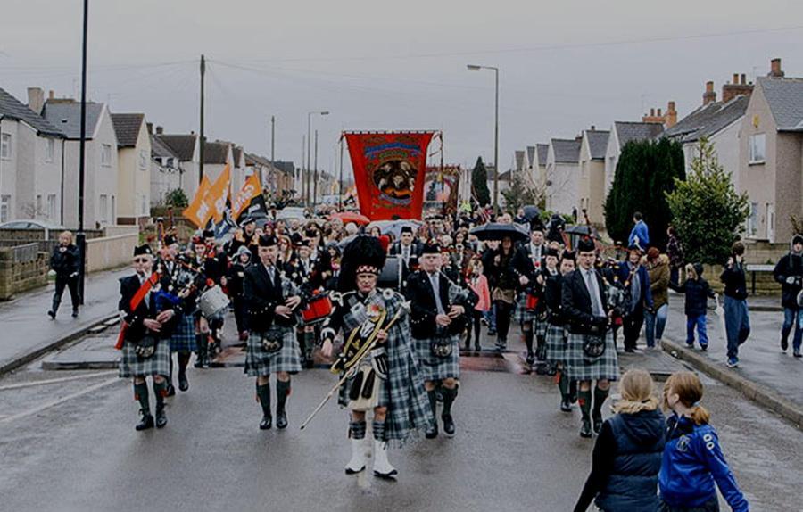 Band playing the bagpipes marching down a road