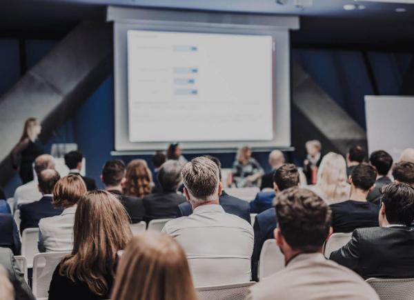 A audience watches a speaker at a conference